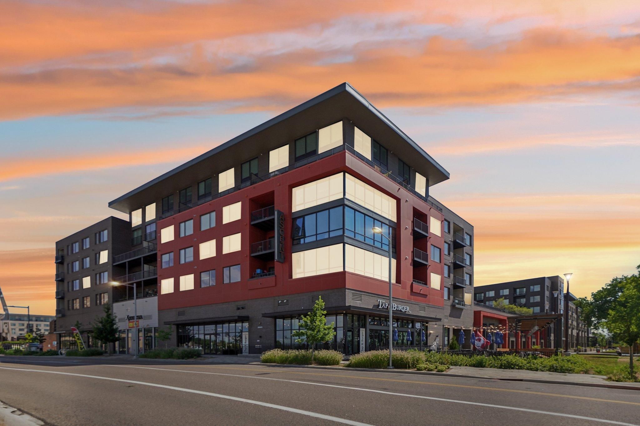 Ascent modern apartment building with red and white facade under a colorful sunset sky, viewed from the street corner.