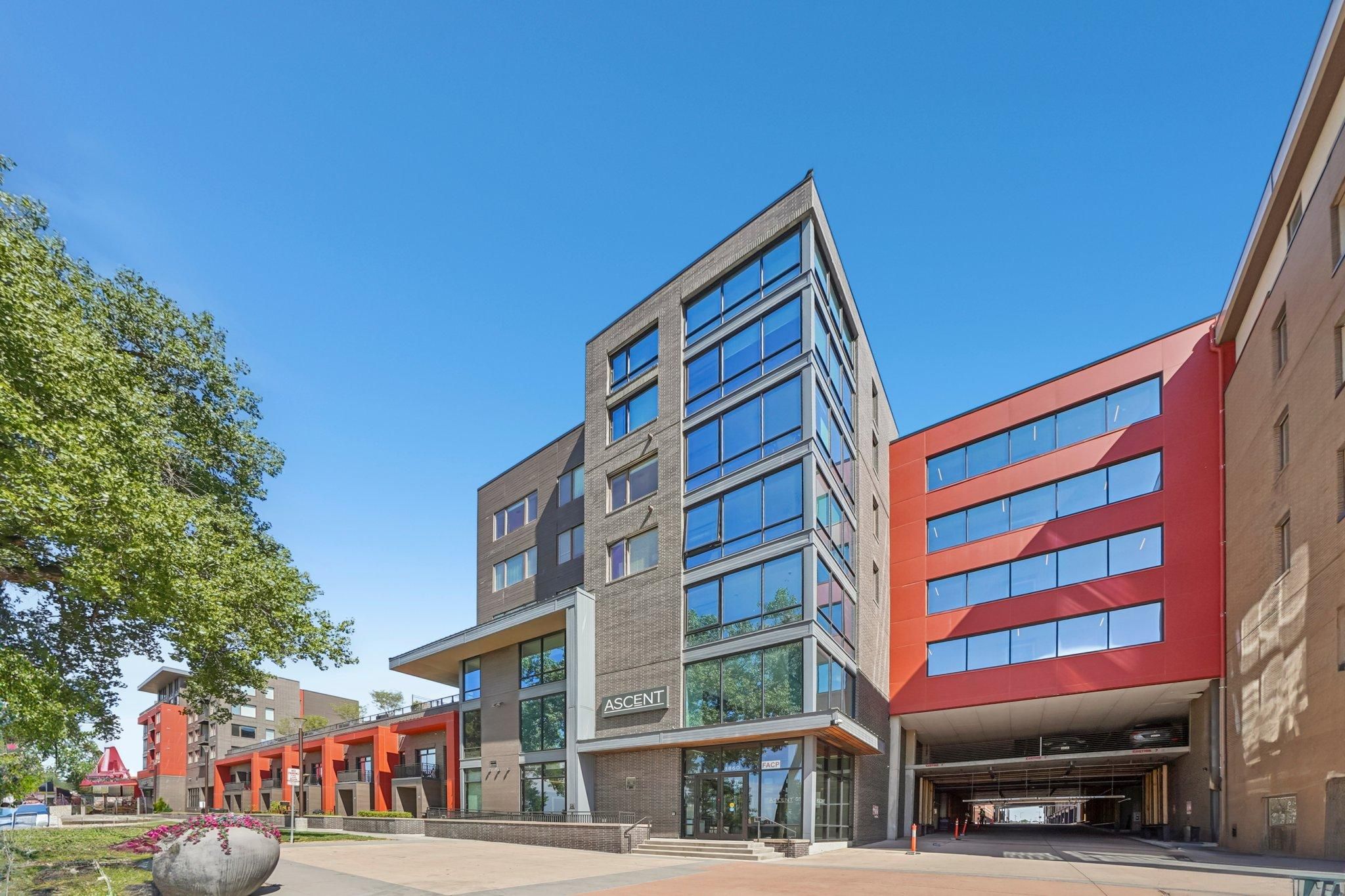 Ascent modern multi-story building with large glass windows and red accents under a clear blue sky.