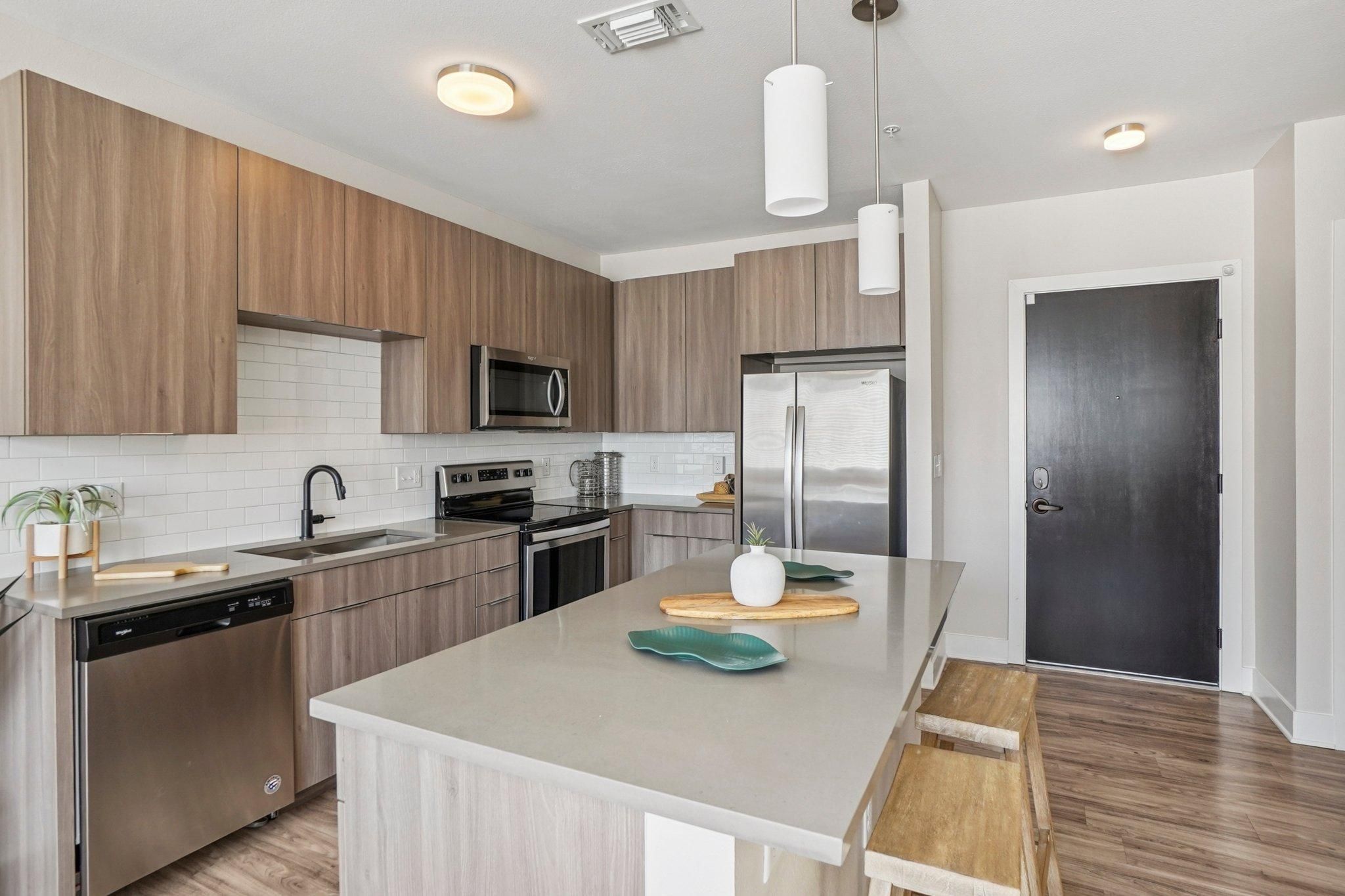 Ascent modern kitchen with wood cabinets, island with stools, stainless appliances, and pendant lights.
