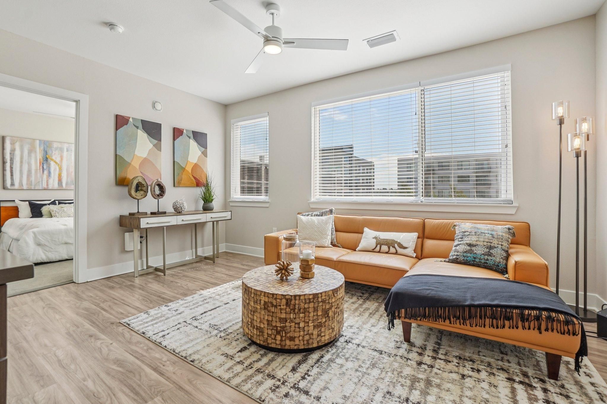 Ascent bright living room with a tan sofa, round wood coffee table, art on the wall, and large windows.