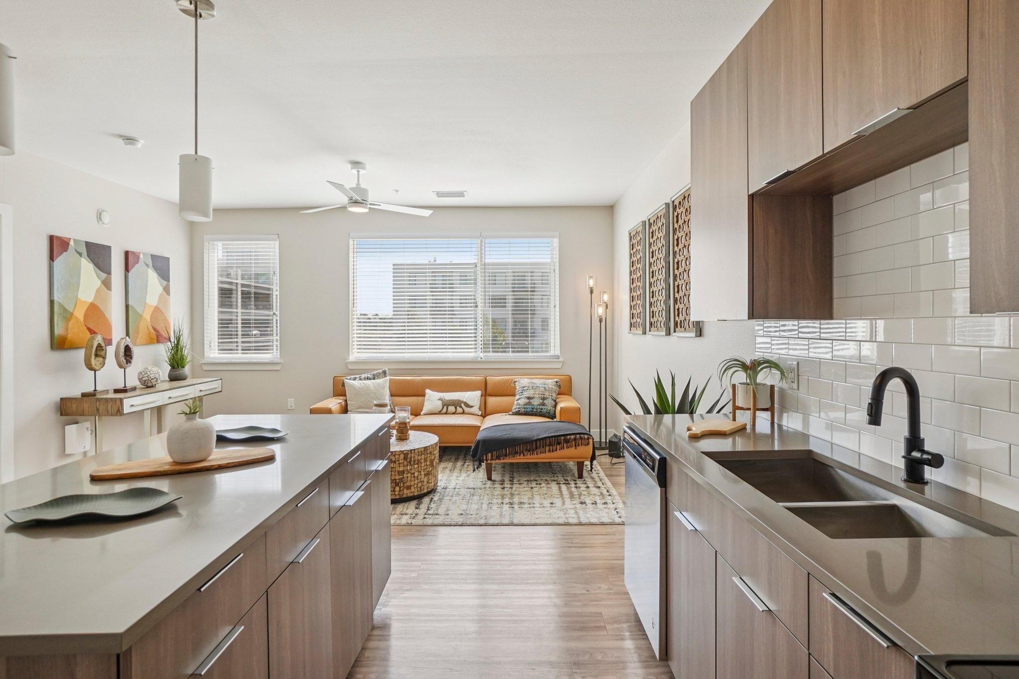 Ascent modern open-plan kitchen and living room with wood cabinets, tan sofa, and large windows letting in natural light.